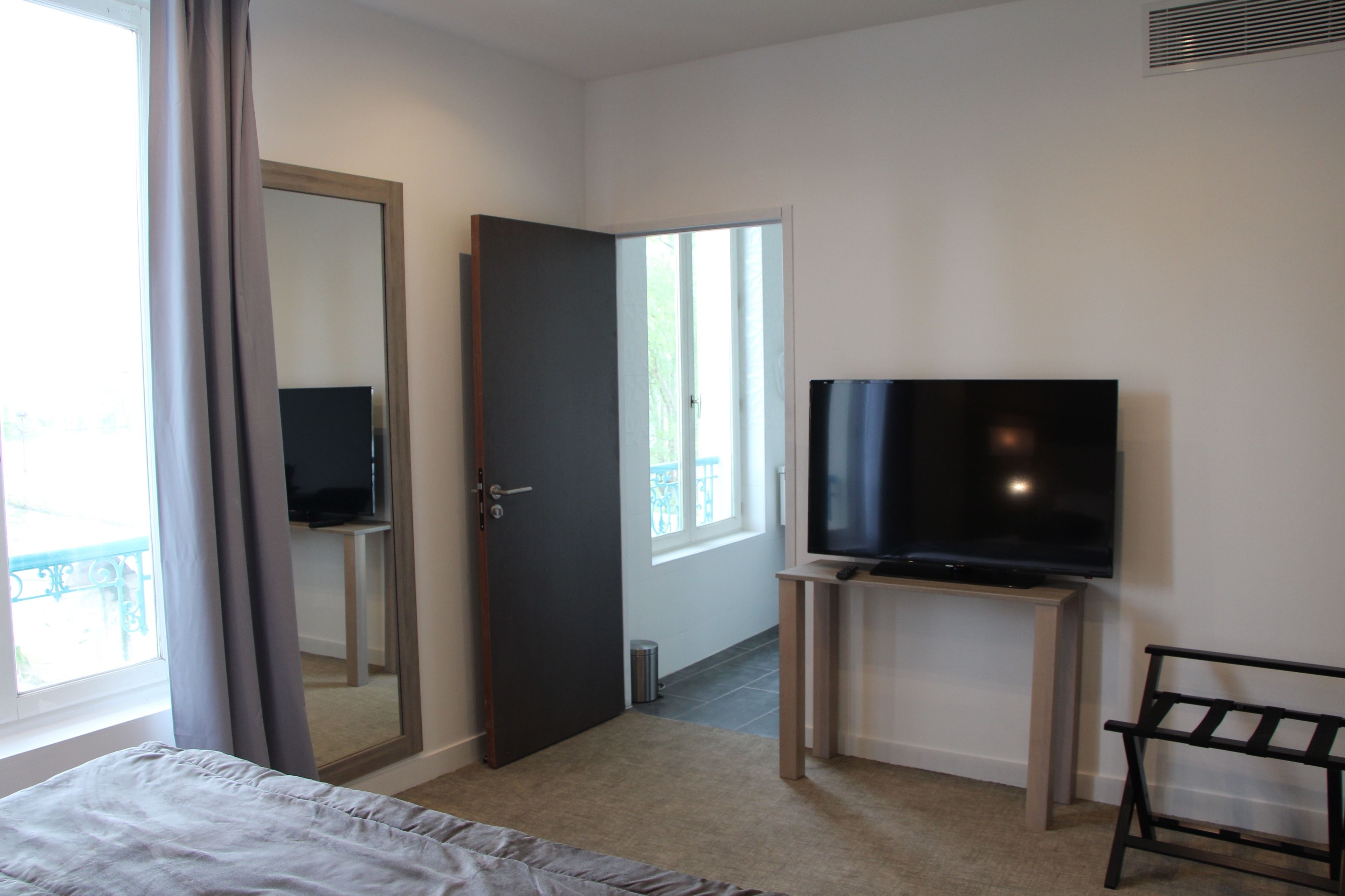 Una habitación de hotel con cama, televisor sobre un mueble, una puerta y una ventana.