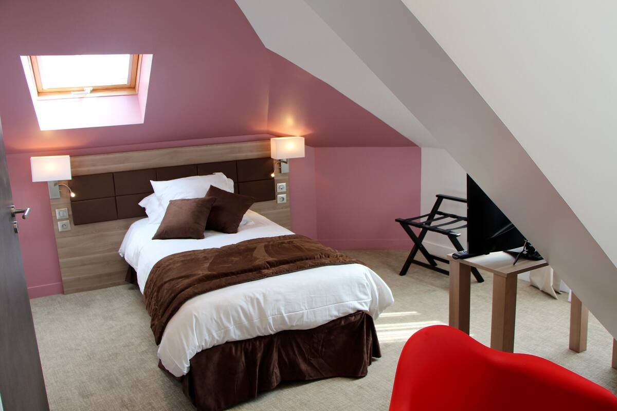 A bedroom with a bed, bedside lamps, a TV, and a red chair.