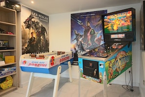 A room with a foosball table, a pinball machine, and a poster of Avengers characters. - Hotel Restaurant L'Esturgeon (Poissy)