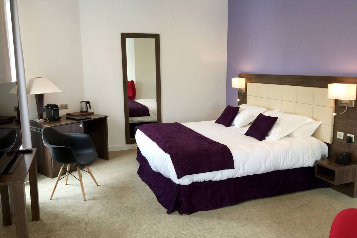 A hotel room with a bed, a desk, a chair, a mirror, and a nightstand.