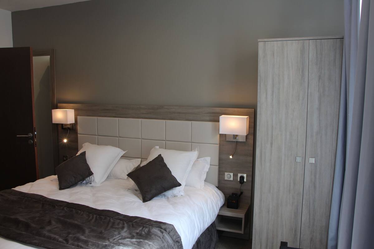 A hotel room with a large bed, two bedside lamps, a wooden wardrobe, and a nightstand with a phone.