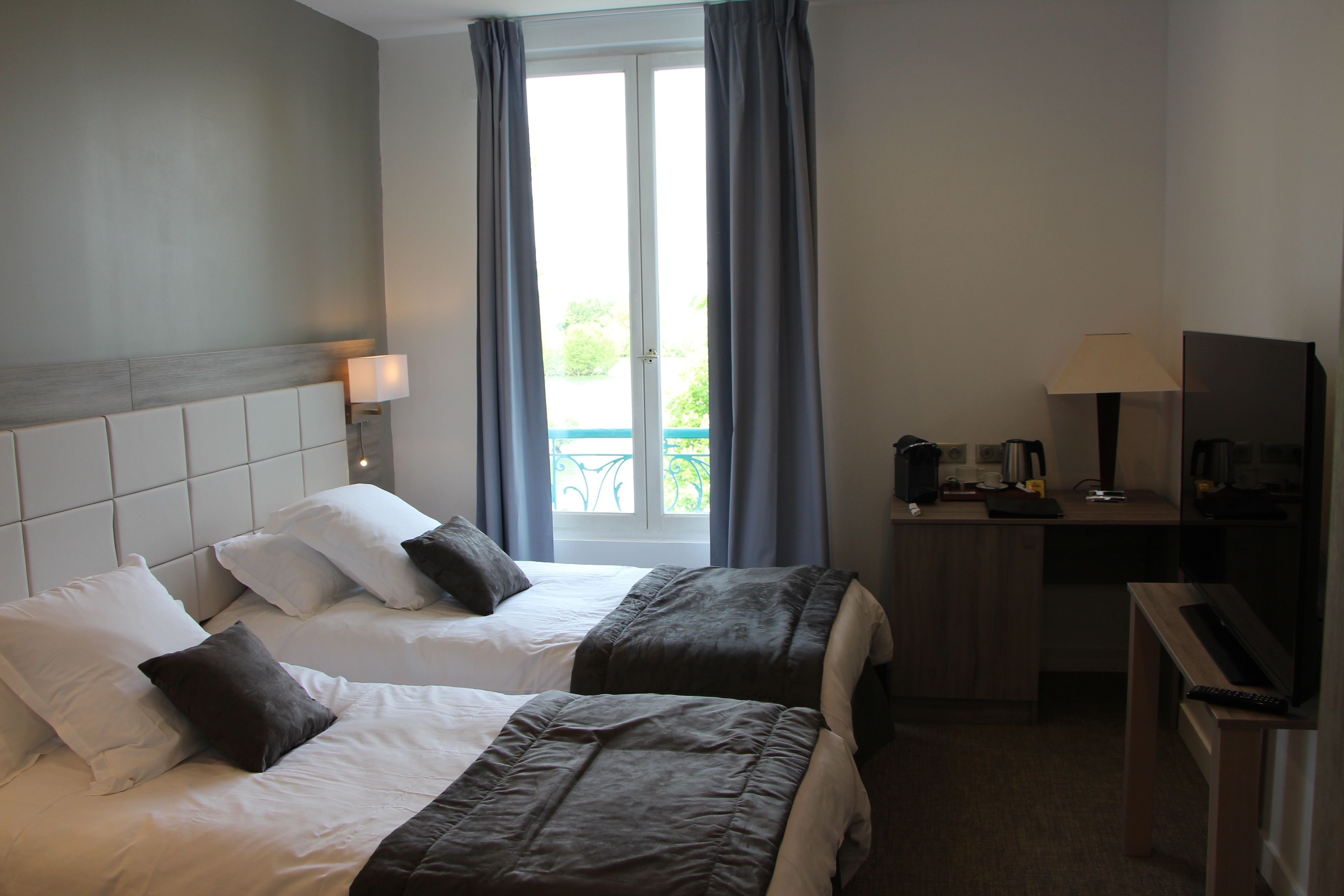 Een hotelkamer met twee bedden, een bureau, een televisie en uitzicht op een balkon.