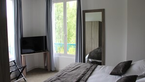 A bedroom with a bed, a TV on a desk, a window with curtains, and a balcony view. - Hotel Restaurant L'Esturgeon (Poissy)