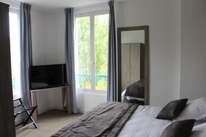 A bedroom with a bed, a TV on a desk, a window with curtains, and a balcony view.