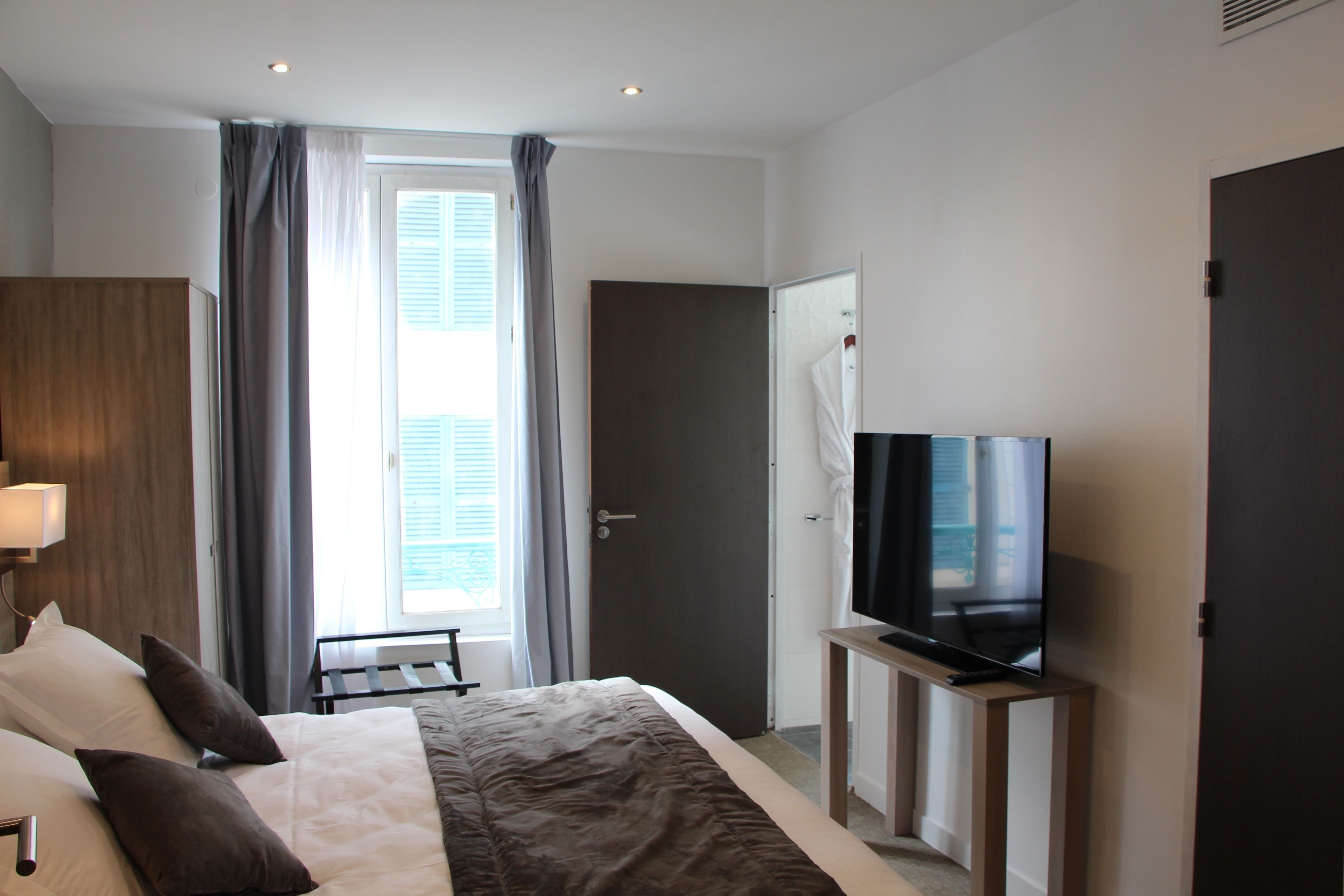 Une chambre d’hôtel avec un lit, un téléviseur posé sur un meuble, un bureau et une fenêtre avec des rideaux.