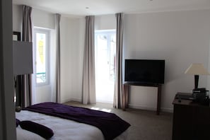 A hotel room with a bed, a television on a stand, a lamp, and a window with curtains. - Hotel Restaurant L'Esturgeon (Poissy)
