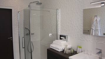 Un baño moderno con cabina de ducha de vidrio, tocador de madera oscura y lavabo blanco.