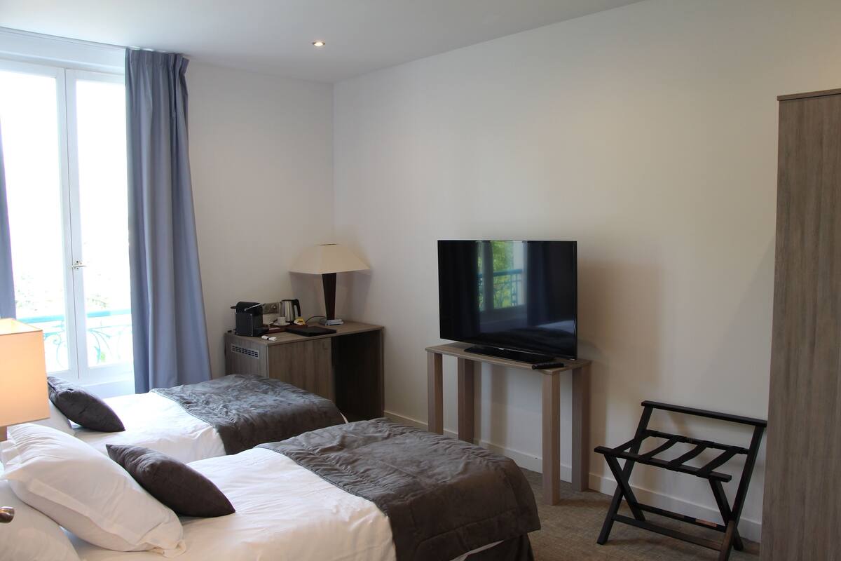 A hotel room with two beds, a TV, a desk with a lamp, and a view of the outdoors.