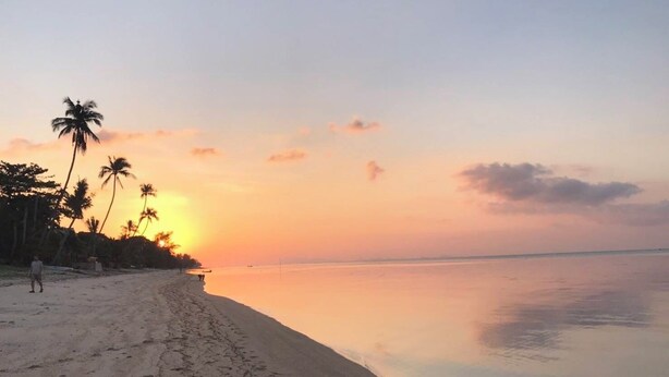 A beach with a calm sea, palm trees, and a sunset. - Krisada Beach Resort (Koh Samui)
