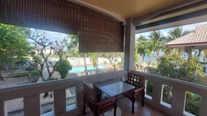 A balcony with a table and chairs, overlooking a swimming pool and palm trees. - Krisada Beach Resort (Koh Samui)