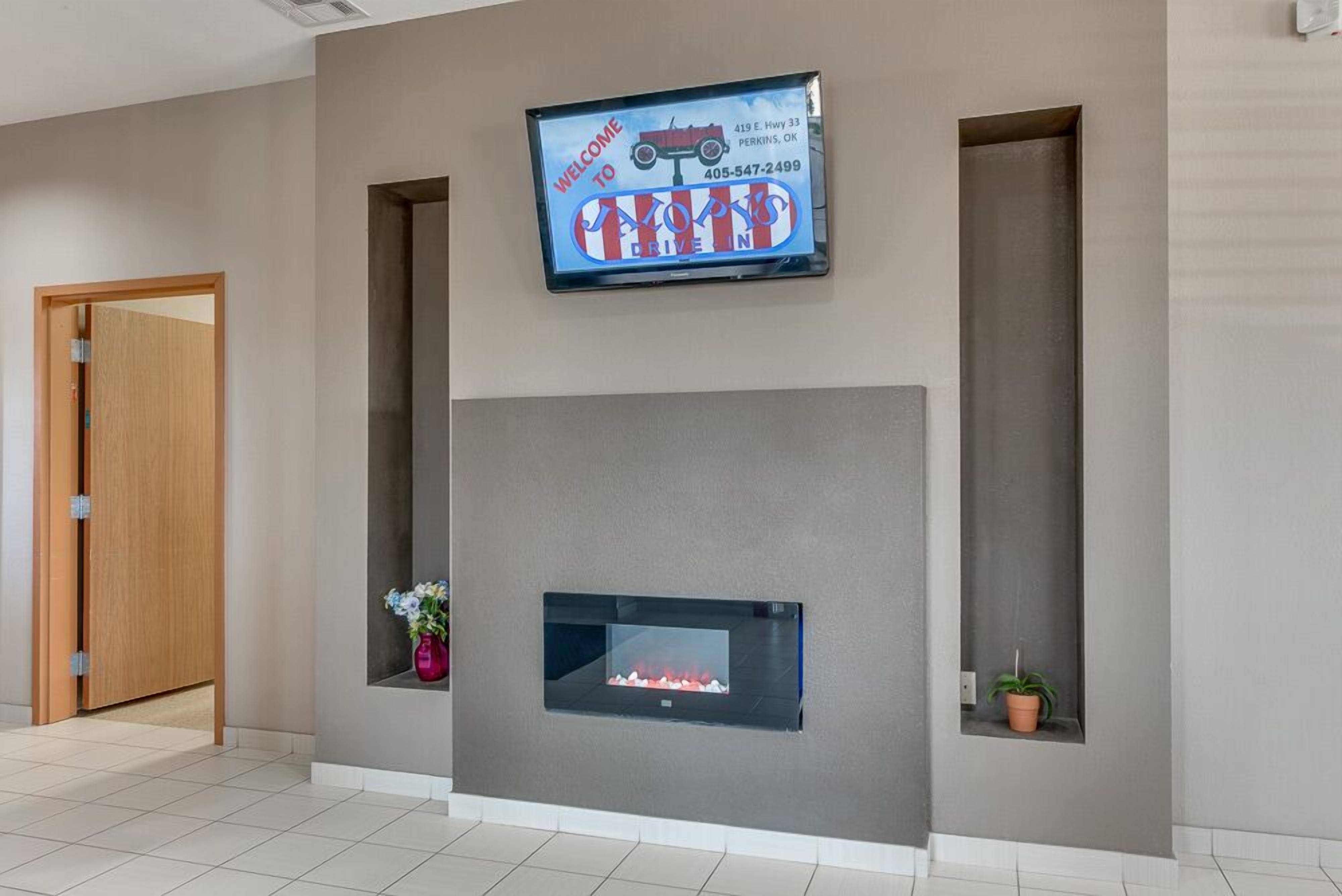 A modern lobby with a flat-screen TV displaying a welcome message, a fireplace, and a potted plant.