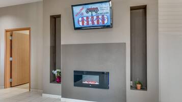 A modern lobby with a flat-screen TV displaying a welcome message, a fireplace, and a potted plant.