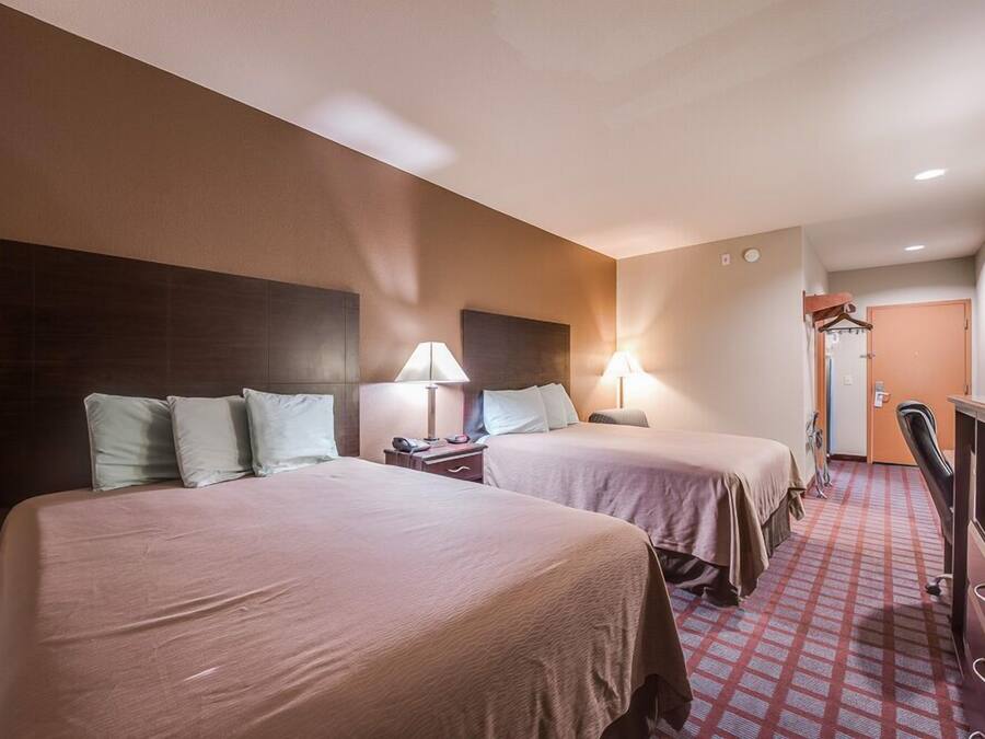 Una habitación de hotel con dos camas, un escritorio, una silla y un armario.