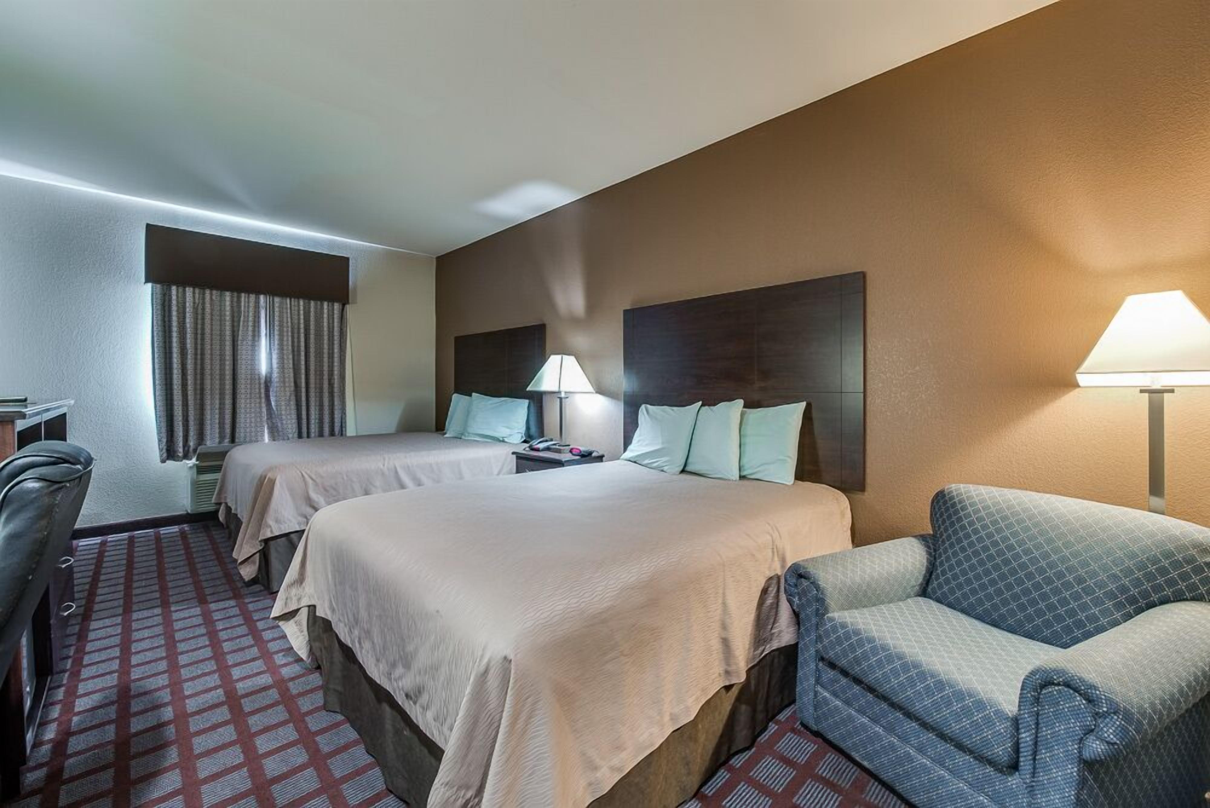 A hotel room with two beds, a desk, a chair, and a sofa.
