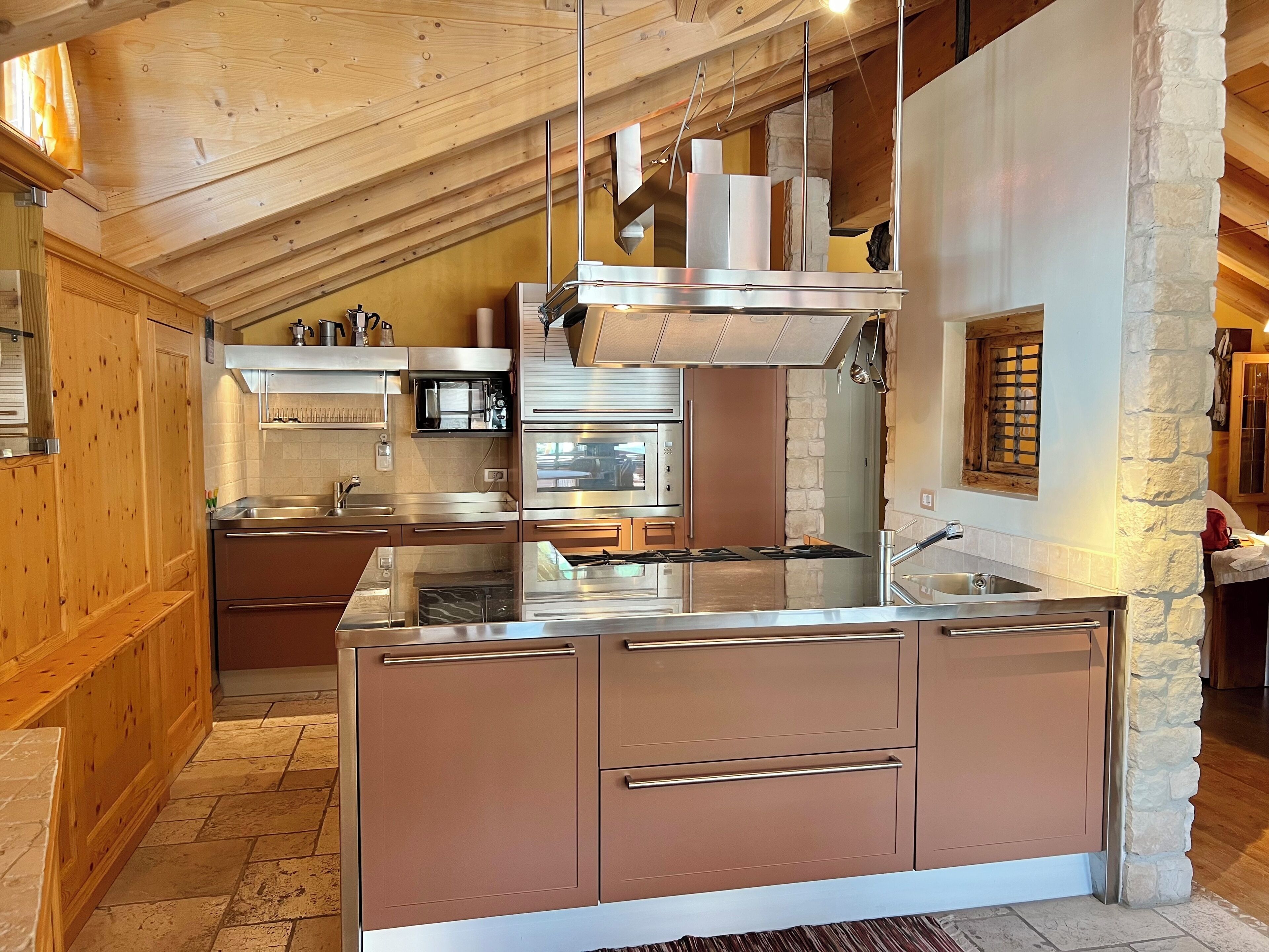 A modern kitchen with wooden ceiling beams, stone accents, and stainless steel appliances.