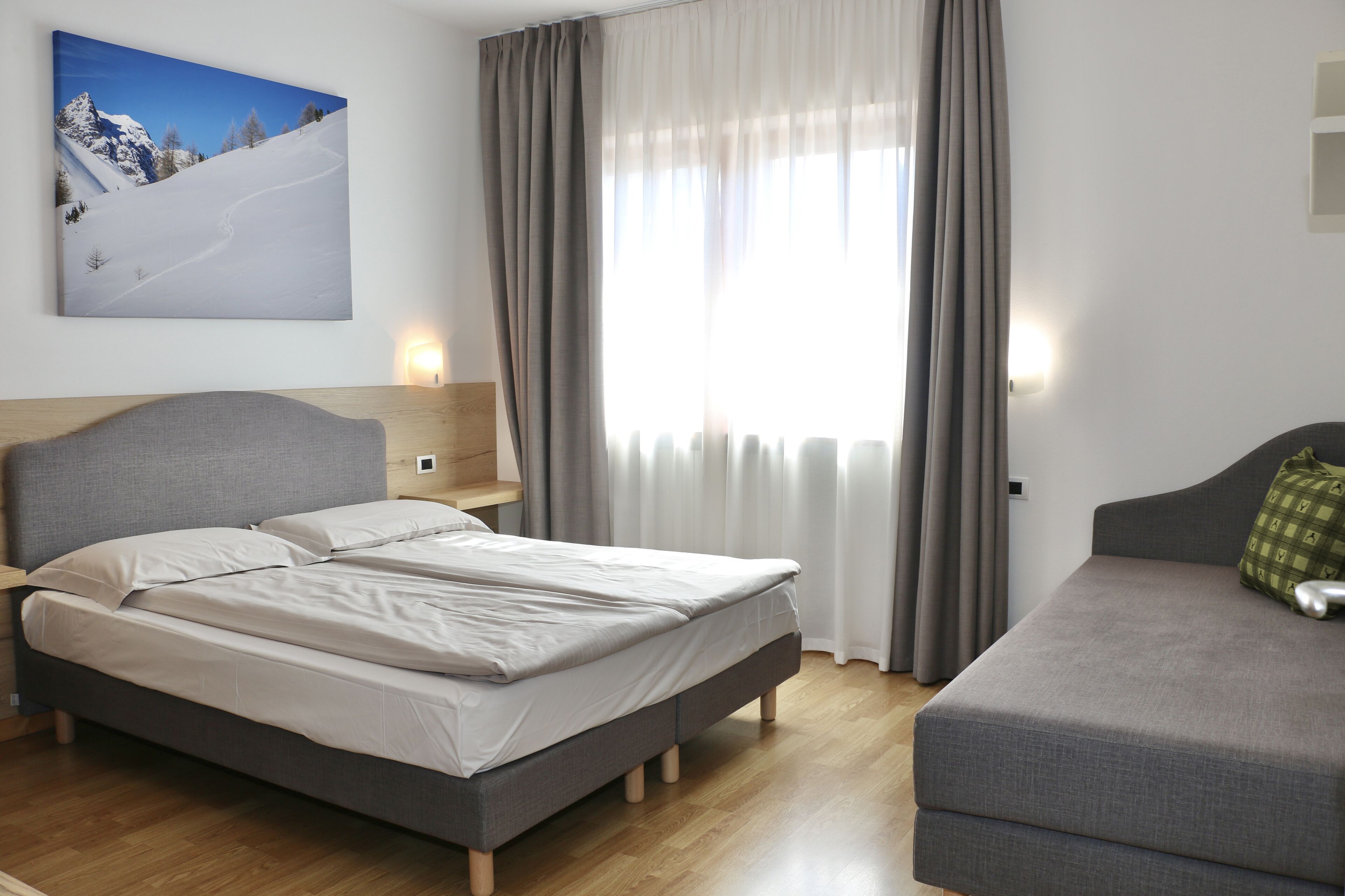 A bedroom with a bed, a sofa, a painting, and a window with curtains.