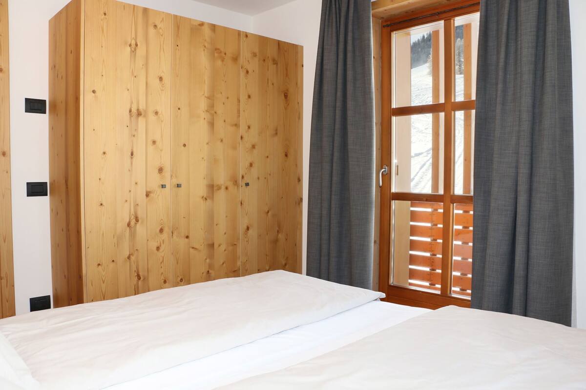 Ein Schlafzimmer mit Holzschrank, Bett und Fenster mit Vorhängen.