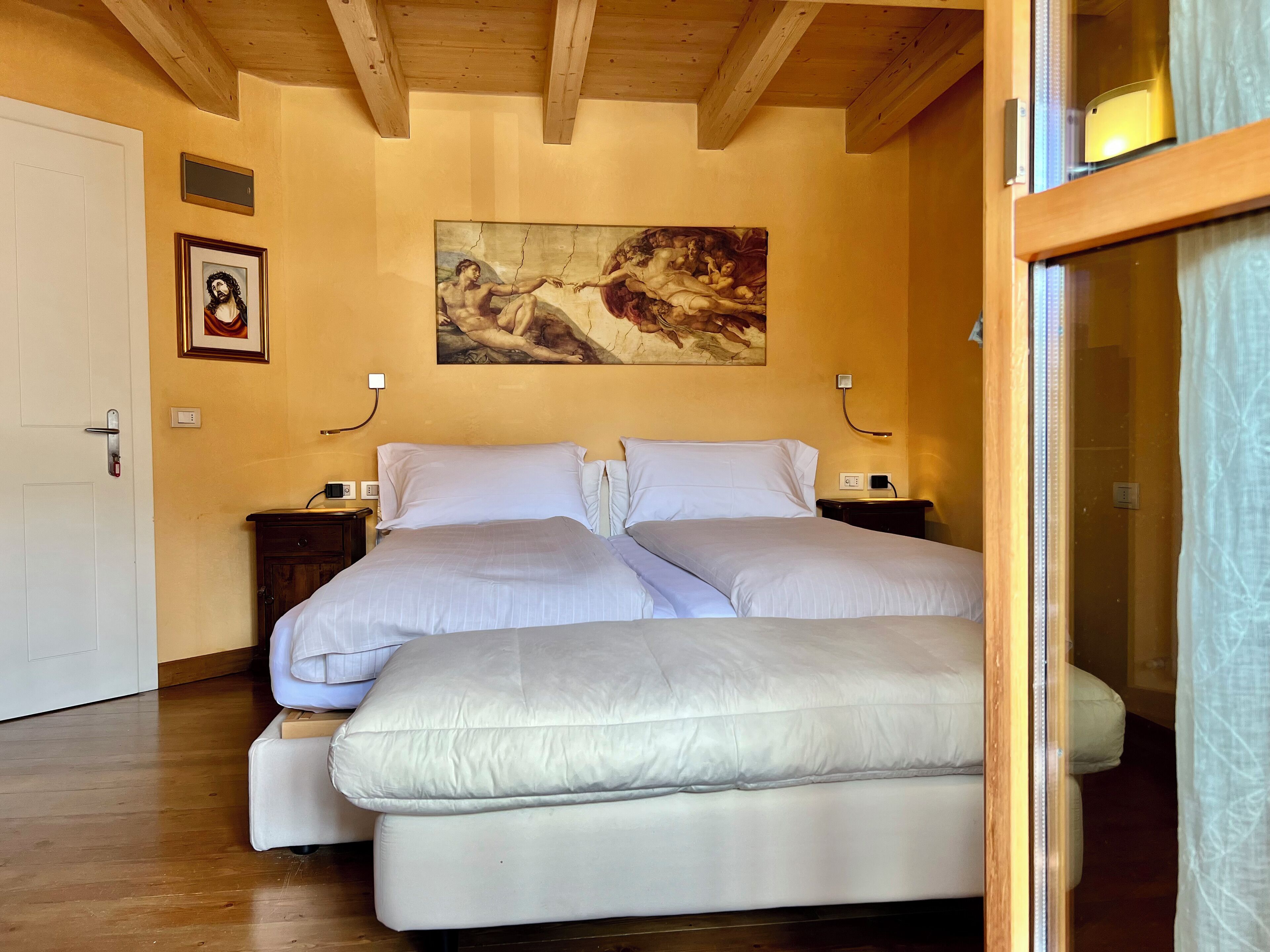 A bedroom with a large bed, wooden ceiling beams, a painting on the wall, and a door.