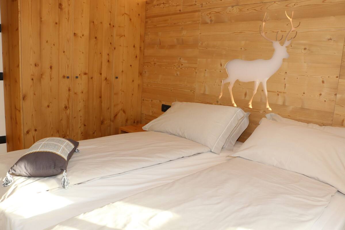 Ein Zimmer mit Holzwänden, einem Bett, Kissen und einer Dekoration mit einem Reh an der Wand.