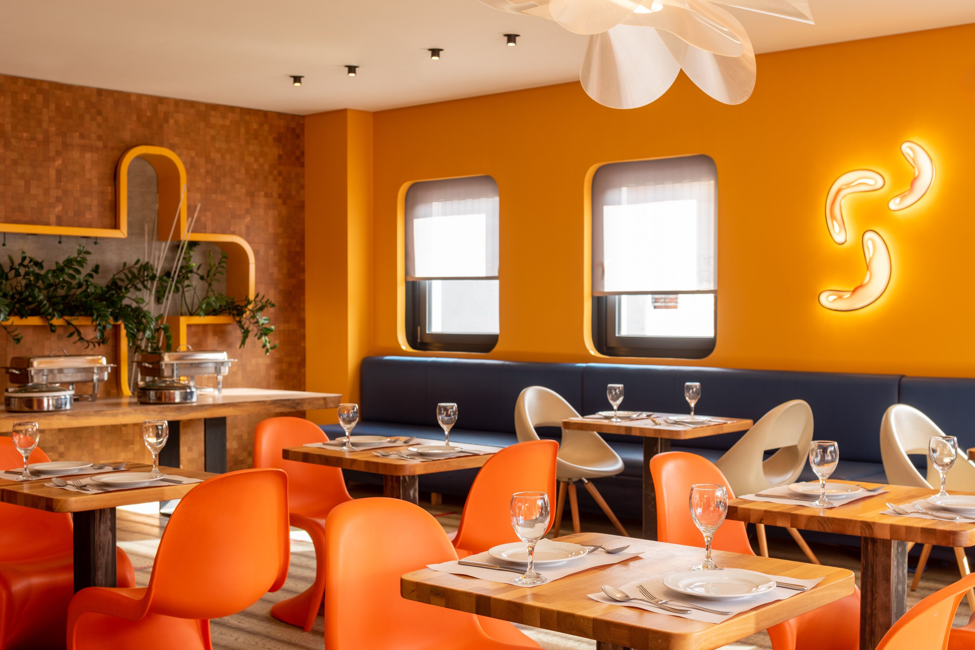Um restaurante com cadeiras e mesas laranja, um sofá azul e uma parede com design em luz neon.