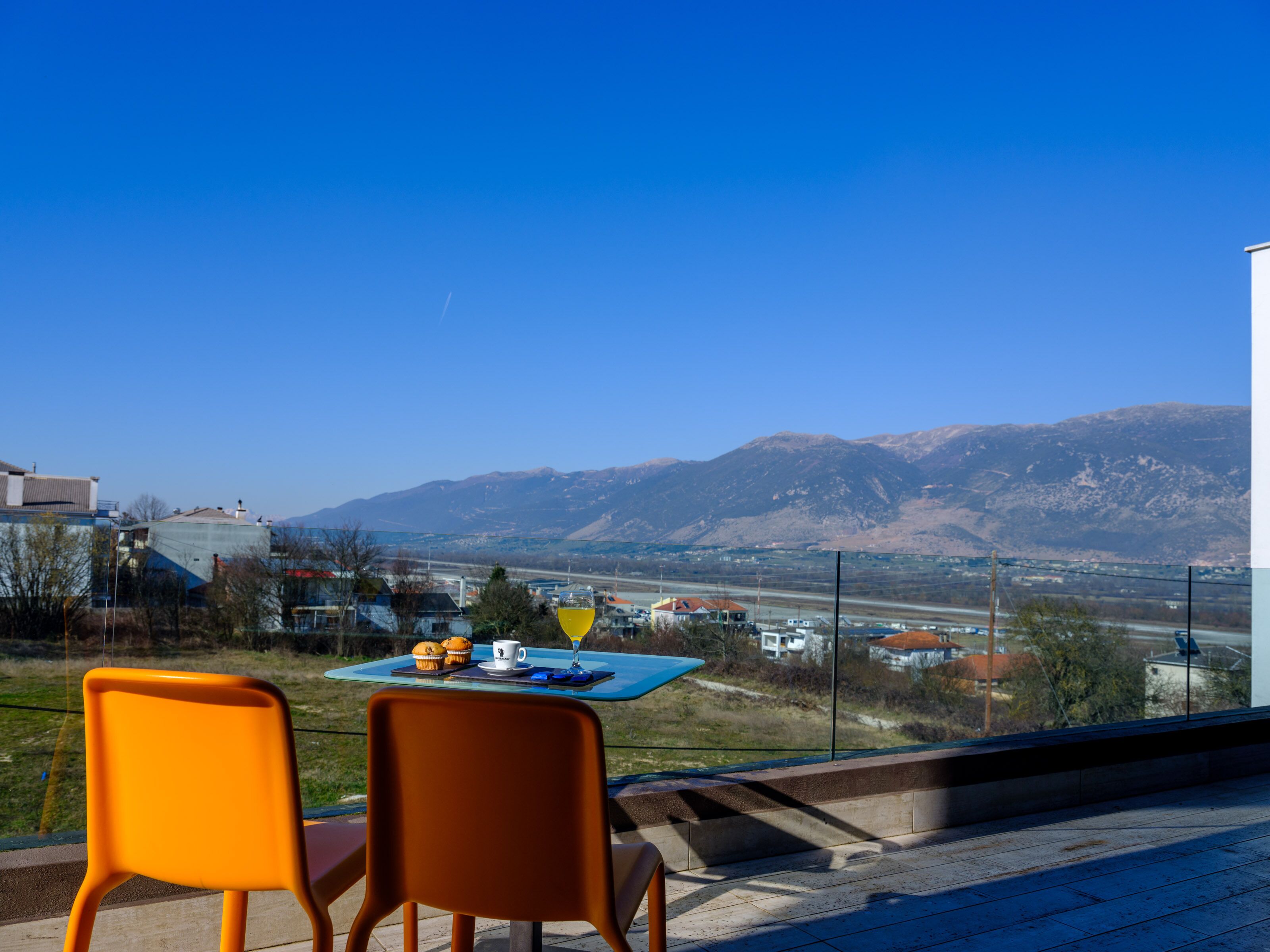 Un balcon avec deux chaises et une table, offrant une vue sur les montagnes et une route.