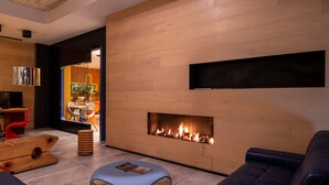 Una sala de estar moderna con chimenea empotrada, televisor de pantalla plana montado en la pared y un área de estar con un pouf azul y un sofá de cuero.