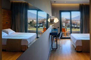 Habitación de hotel con dos camas, un escritorio y vistas a un paisaje montañoso.