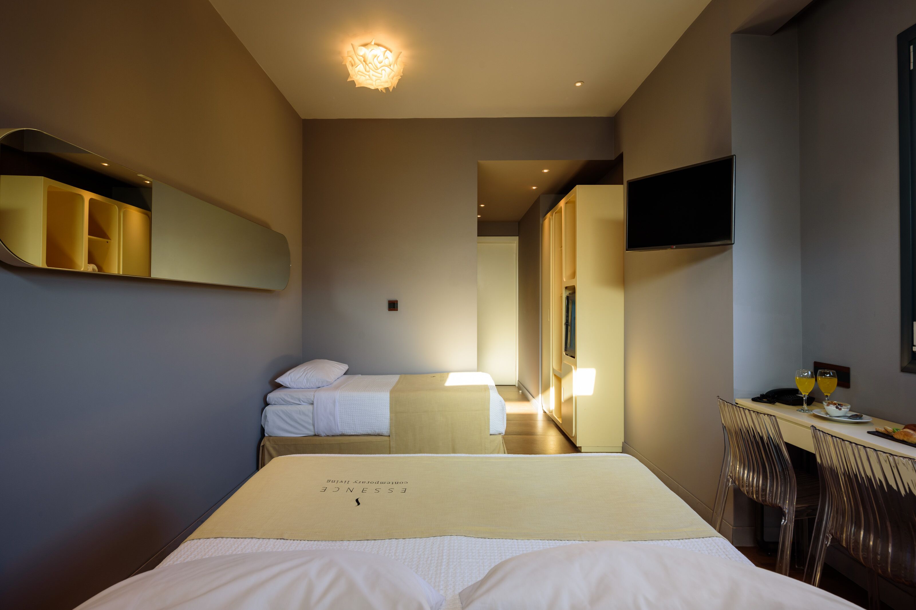 A hotel room with two beds, a desk with chairs, a flat-screen TV, and a mirror.