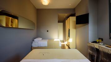 A hotel room with two beds, a desk with chairs, a flat-screen TV, and a mirror.