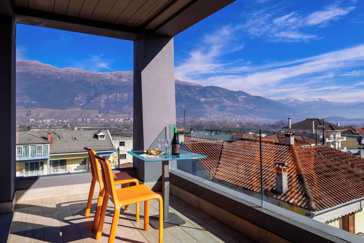 Un balcón con mesa y sillas, con vistas a un paisaje montañoso y edificios residenciales.