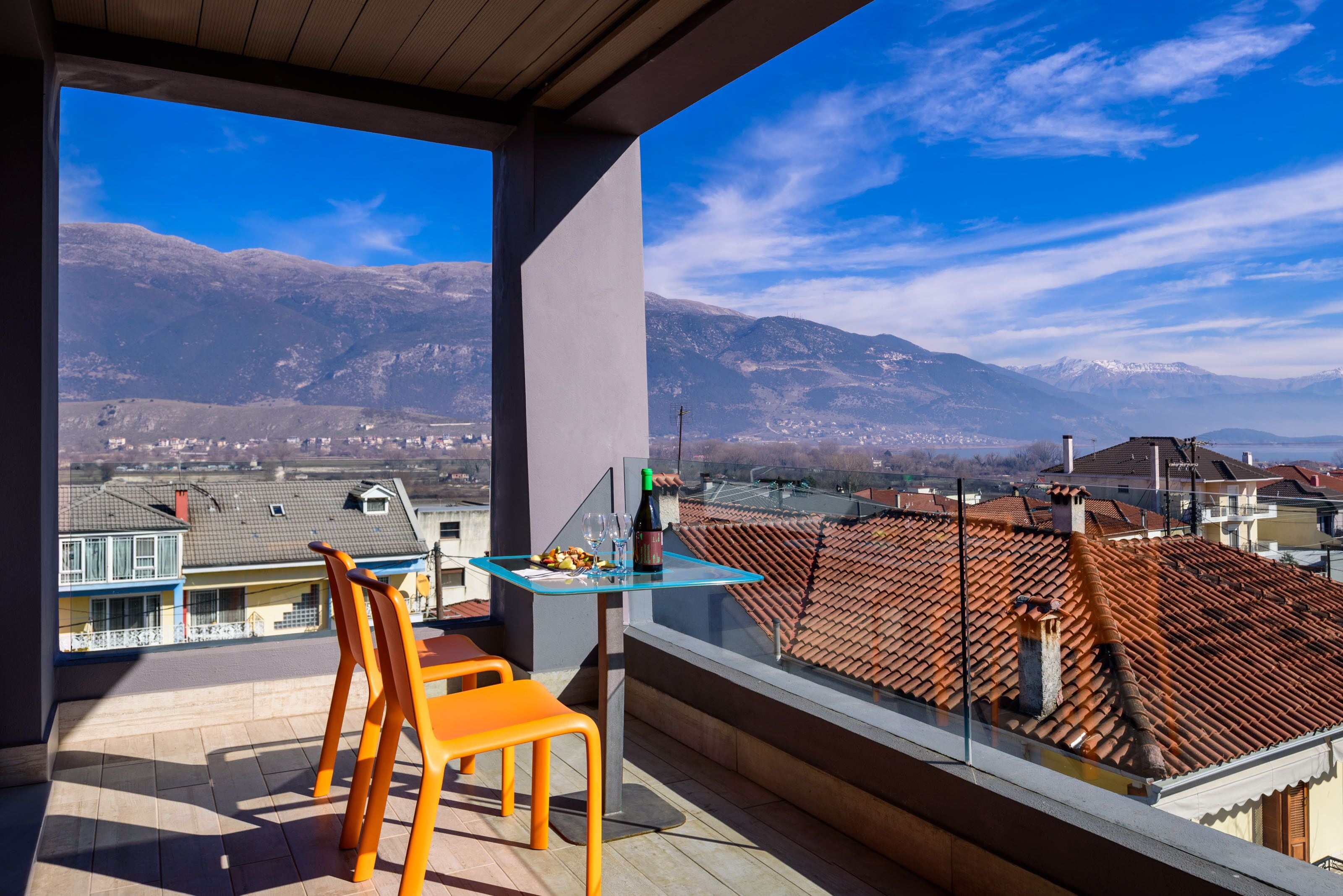 A balcony with a table and chairs, overlooking a mountainous landscape with residential buildings.