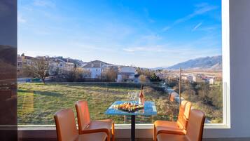 A dining area with a table set for two, overlooking a residential neighborhood and mountains.
