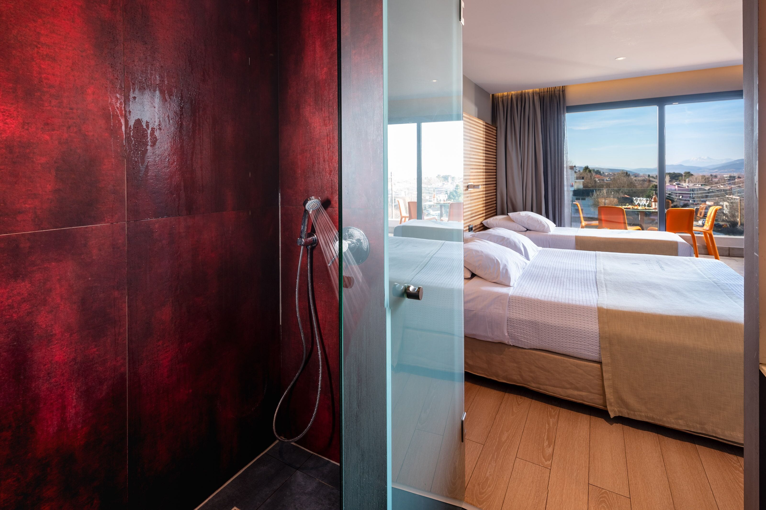 A modern hotel room with a large bed, a shower area, and a balcony with a city view.