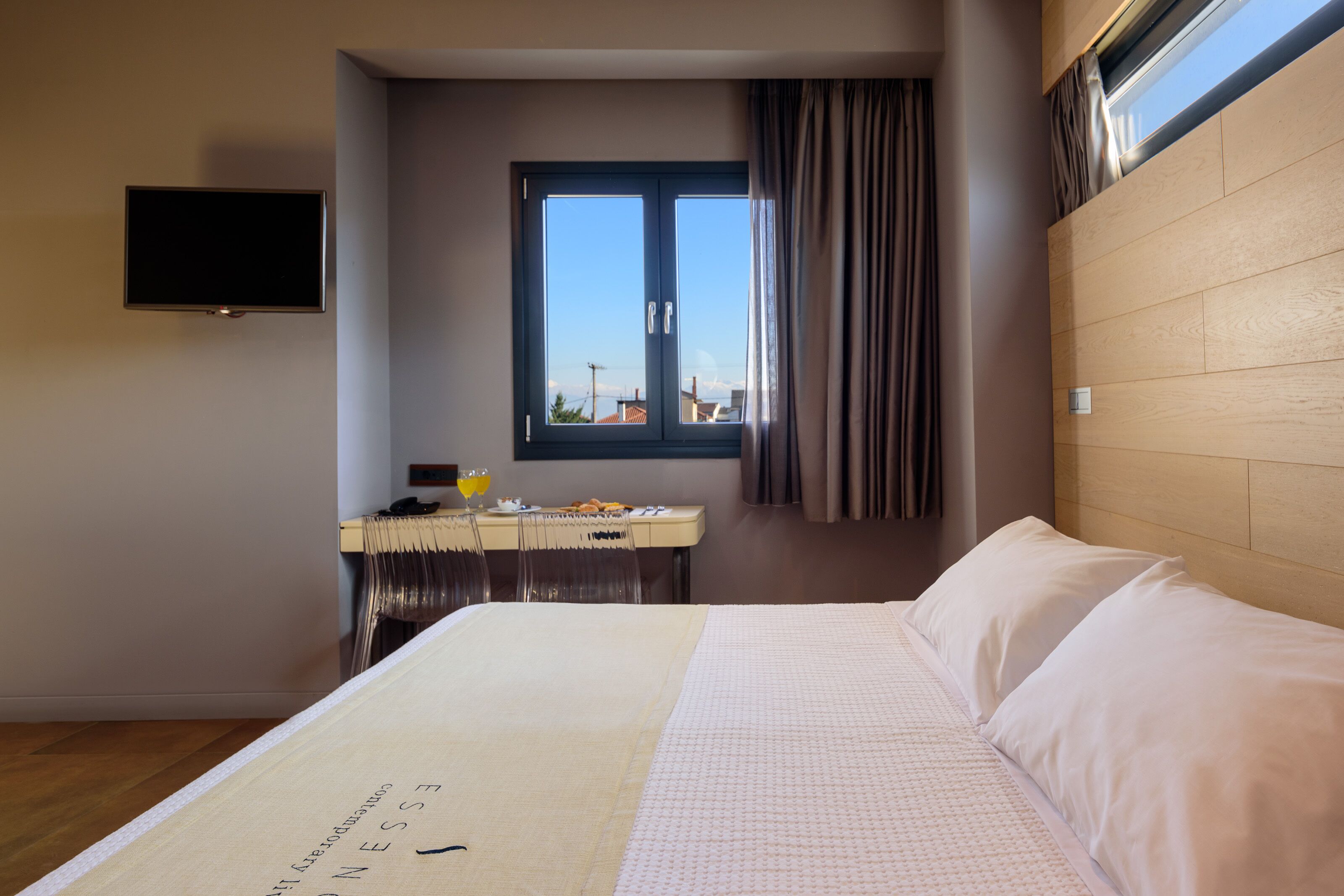 Une chambre d’hôtel comprenant un lit, un bureau avec une chaise, un téléviseur fixé au mur et une fenêtre avec des rideaux.