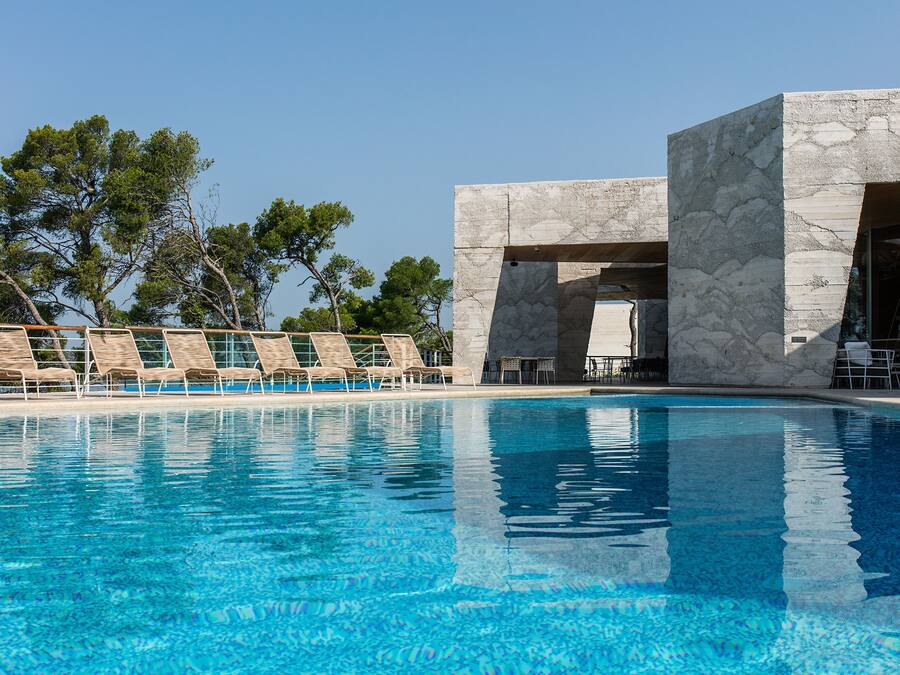 A swimming pool with lounge chairs and a stone building with large windows.