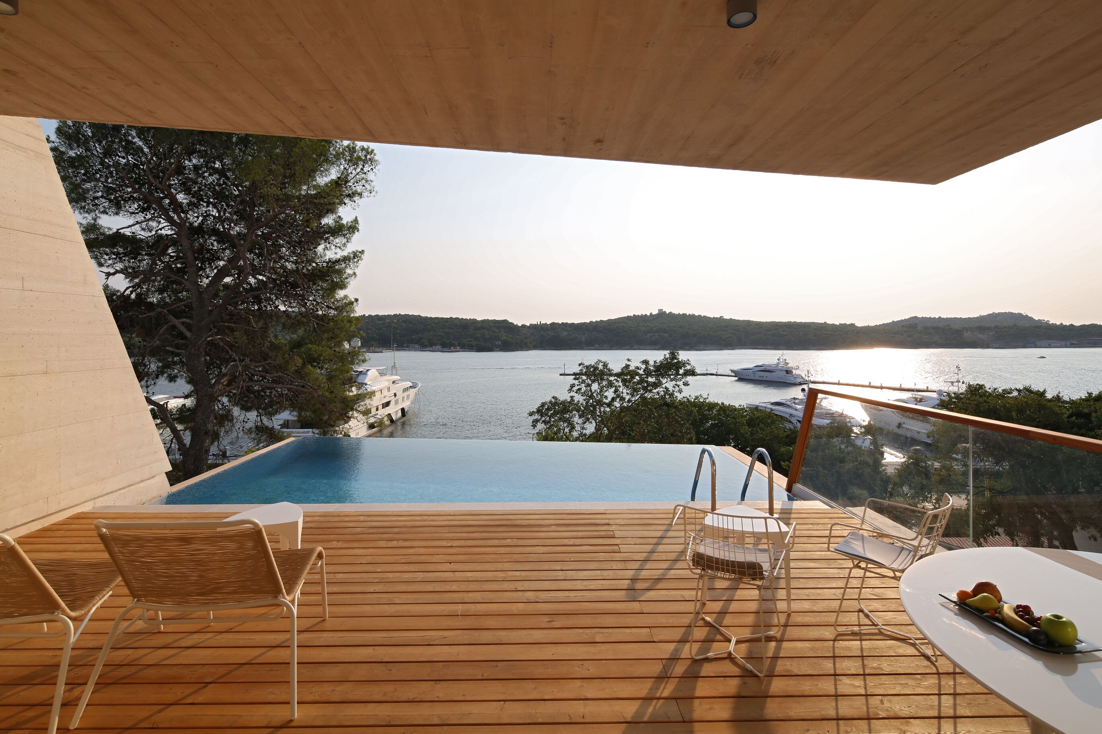 Ein Infinity-Pool mit Holzterrasse, Liegestühlen und einem Tisch mit Obst.