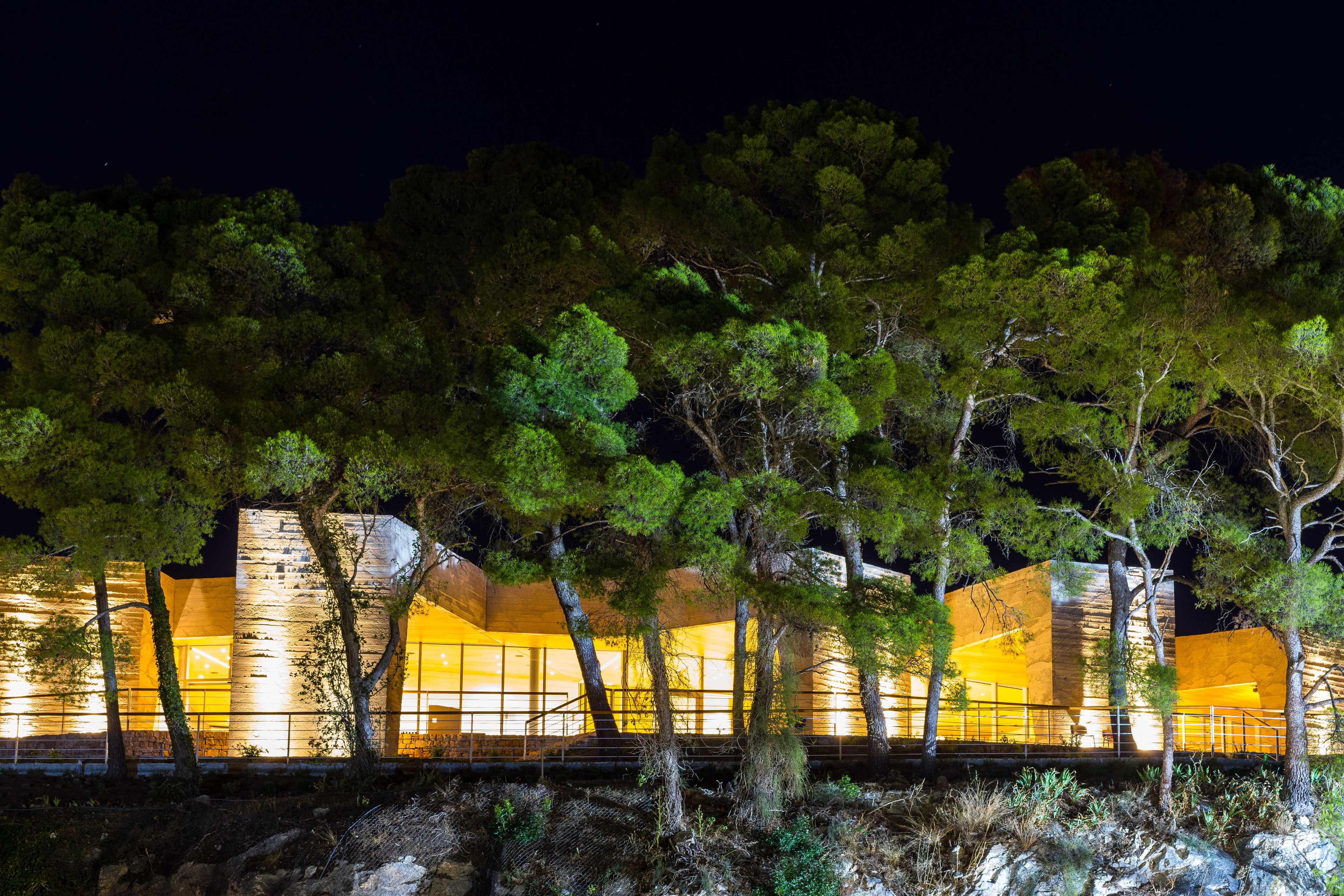 A modern building with large windows and a stone facade, surrounded by trees.