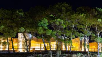 A modern building with large windows and a stone facade, surrounded by trees.