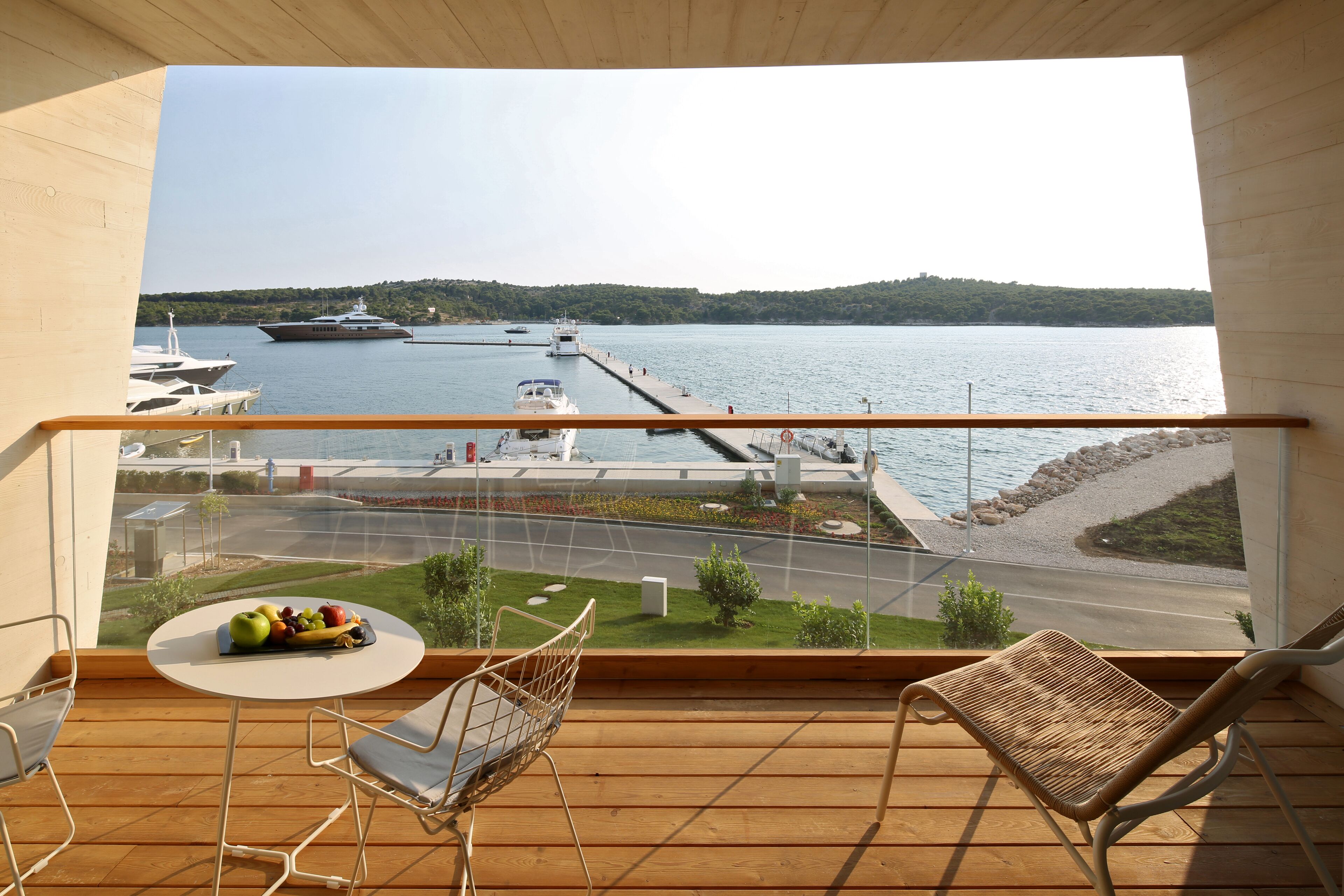 A balcony with a view of a marina, a table with fruit, and two chairs.