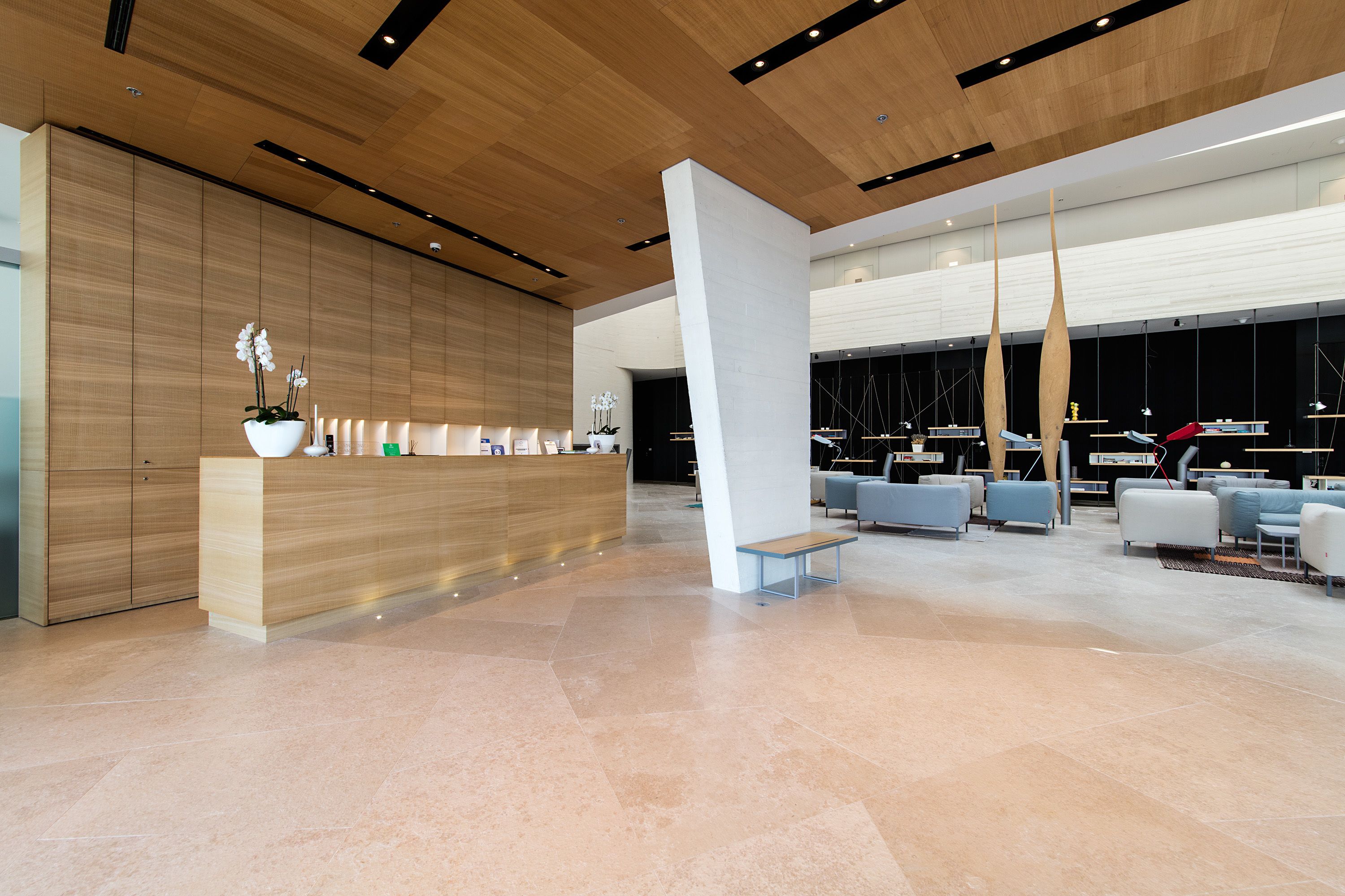 Eine moderne Lobby mit einer Rezeption, einer Sitzecke und einer hohen Decke mit Holzpaneelen.