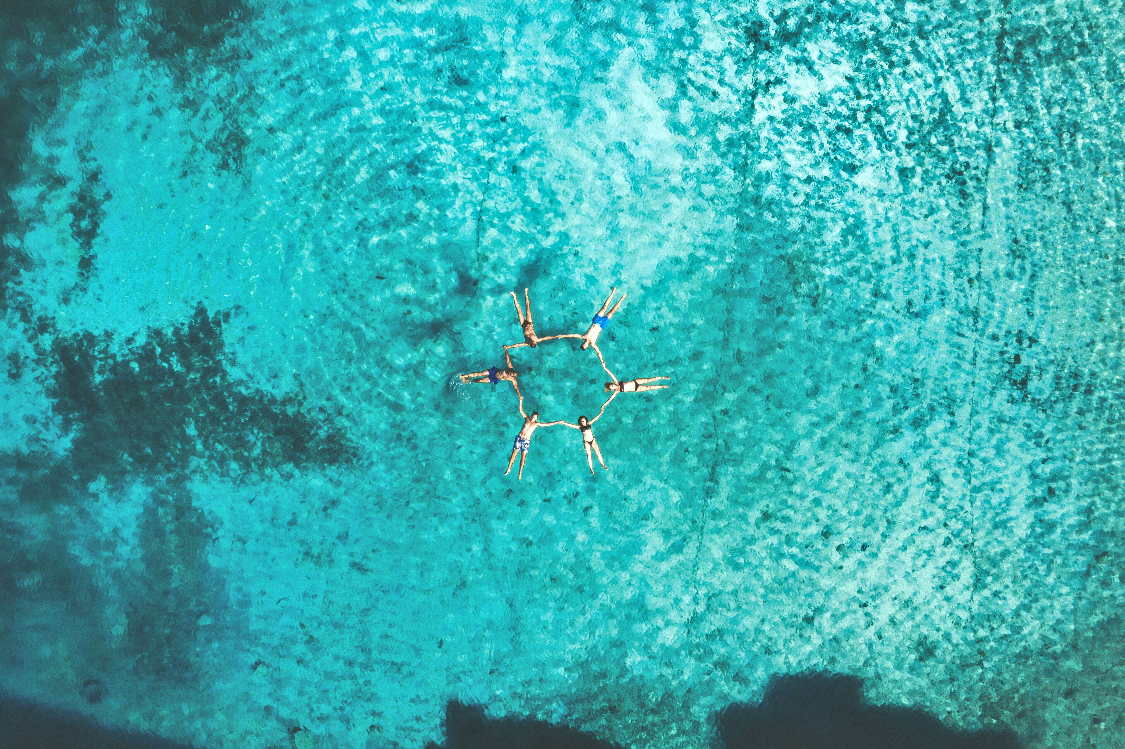 Ovenudblik over en turkis strand med en cirkelformet samling af mennesker.