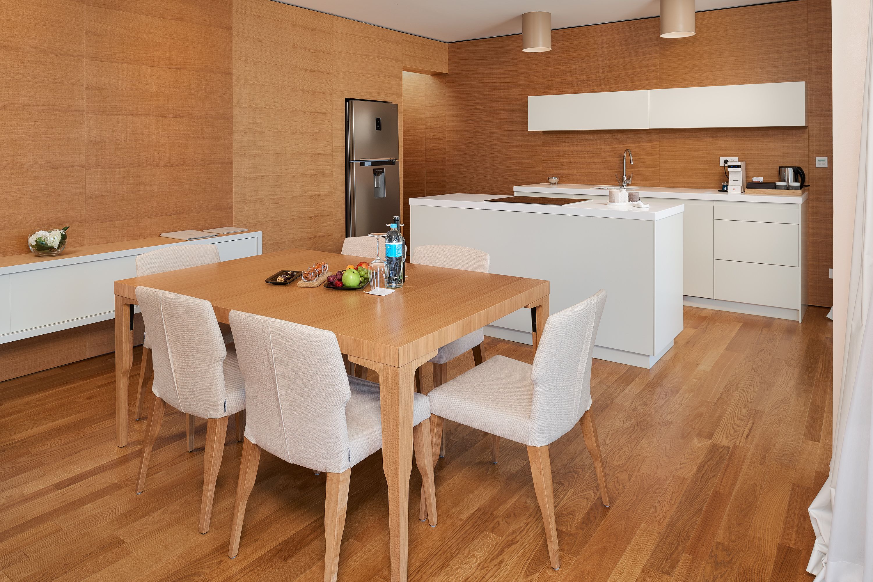 Eine moderne Küche mit einem Holztisch, weißen Stühlen und einem Einbaukühlschrank.