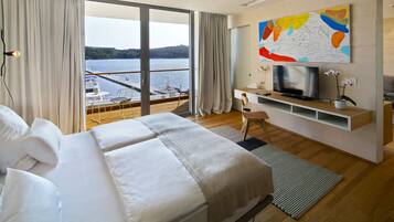 A modern hotel room with a large bed, a TV, a desk, and a view of a lake.