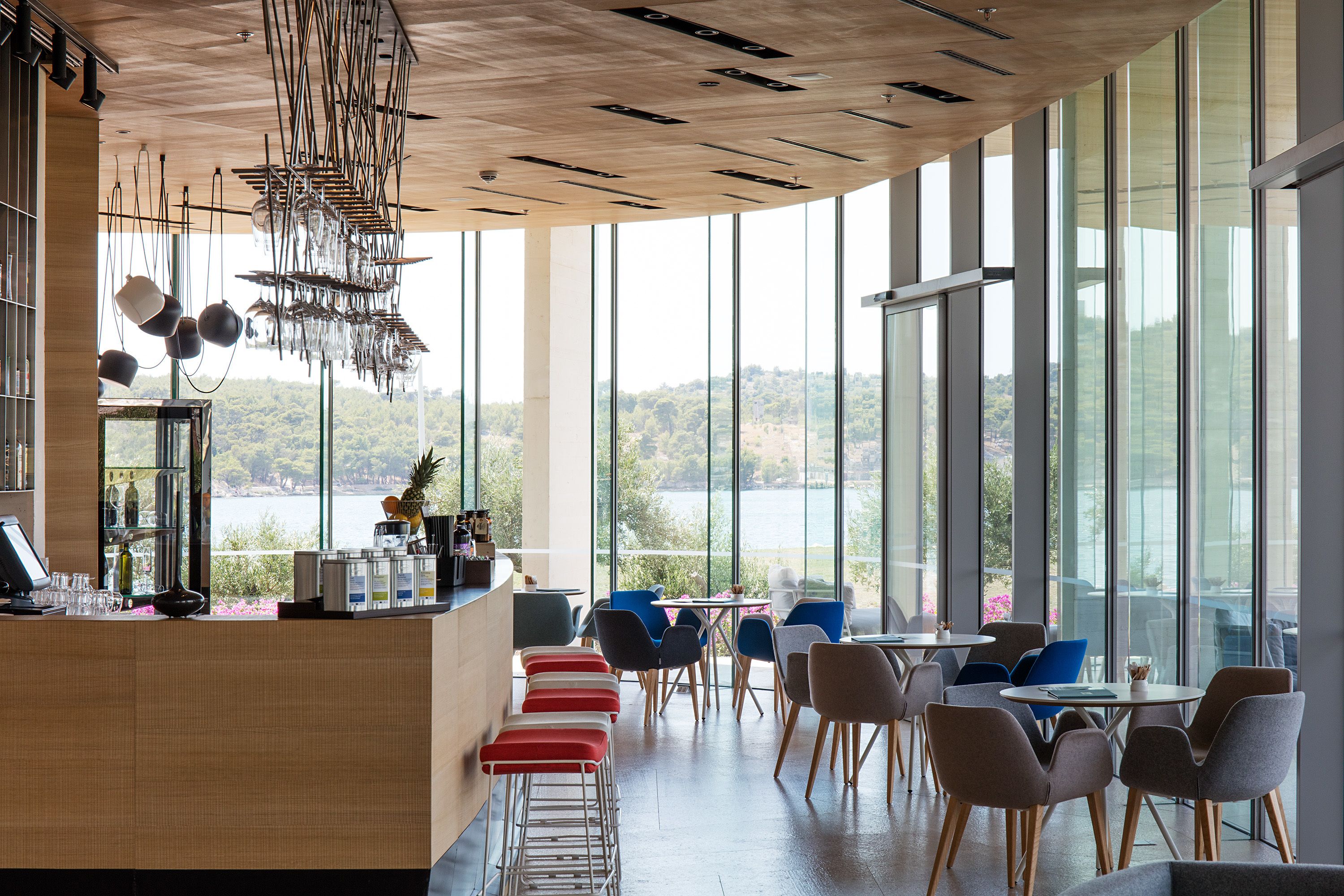A modern restaurant with a wooden ceiling, large windows, and a view of a lake.