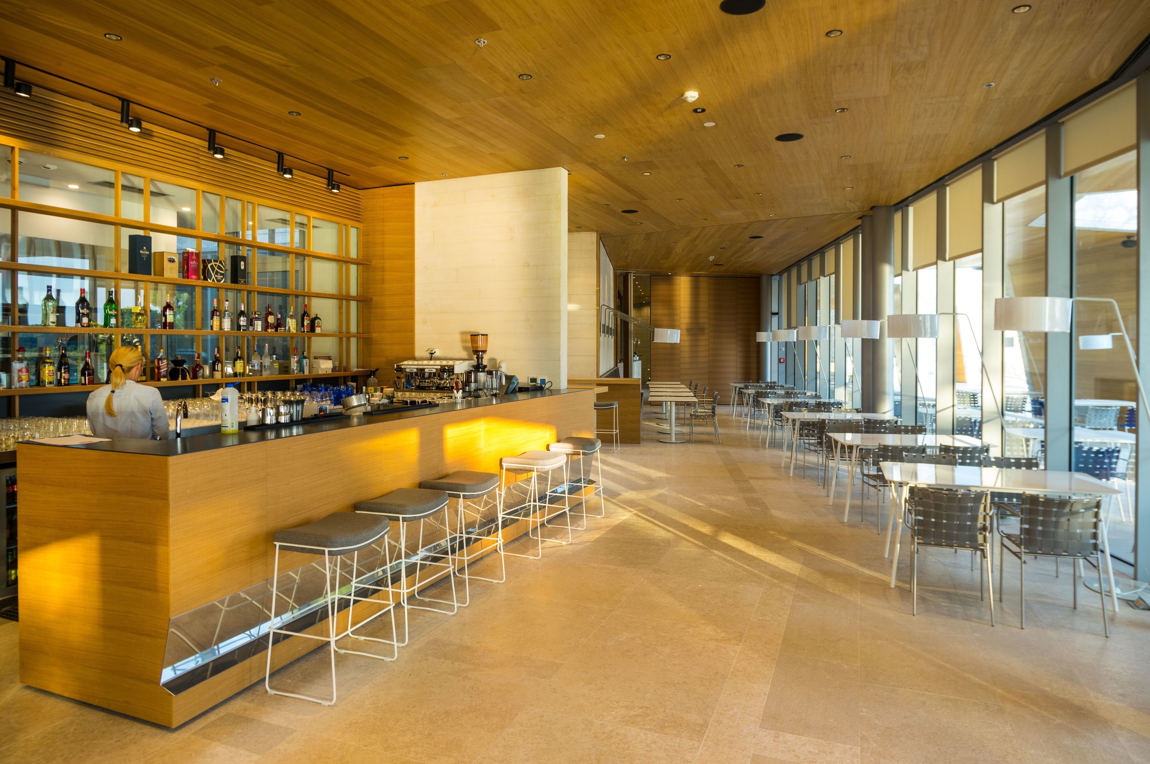 Un área de bar moderna con mostrador de madera, taburetes y una vitrina de botellas.