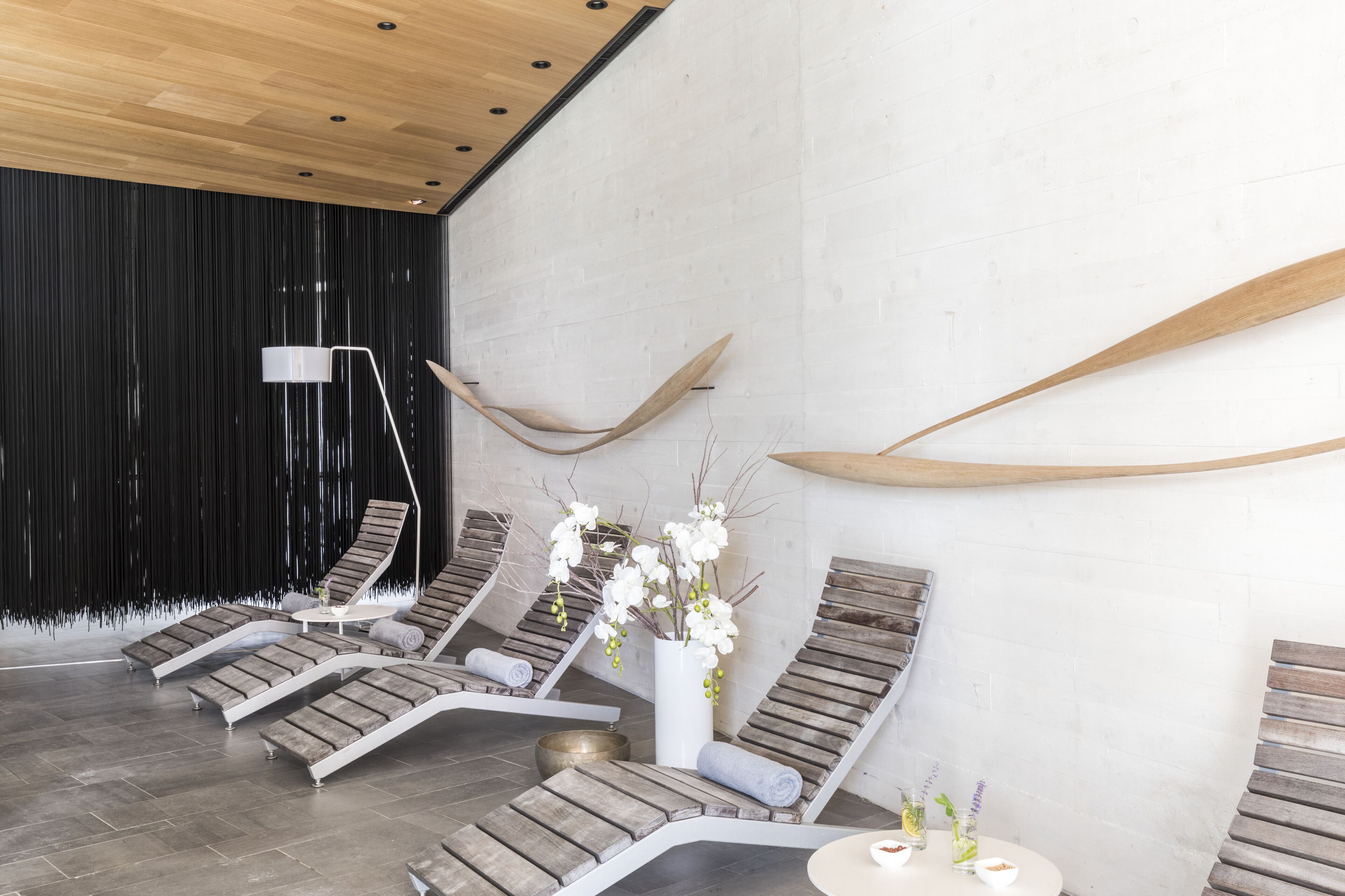 A spa area with wooden lounge chairs, a white vase with flowers, and a large wooden surfboard on the wall.