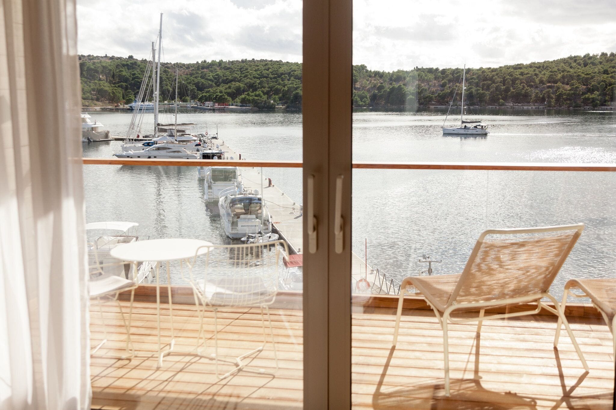 A balcony with a view of a marina, including boats and a forested hillside.