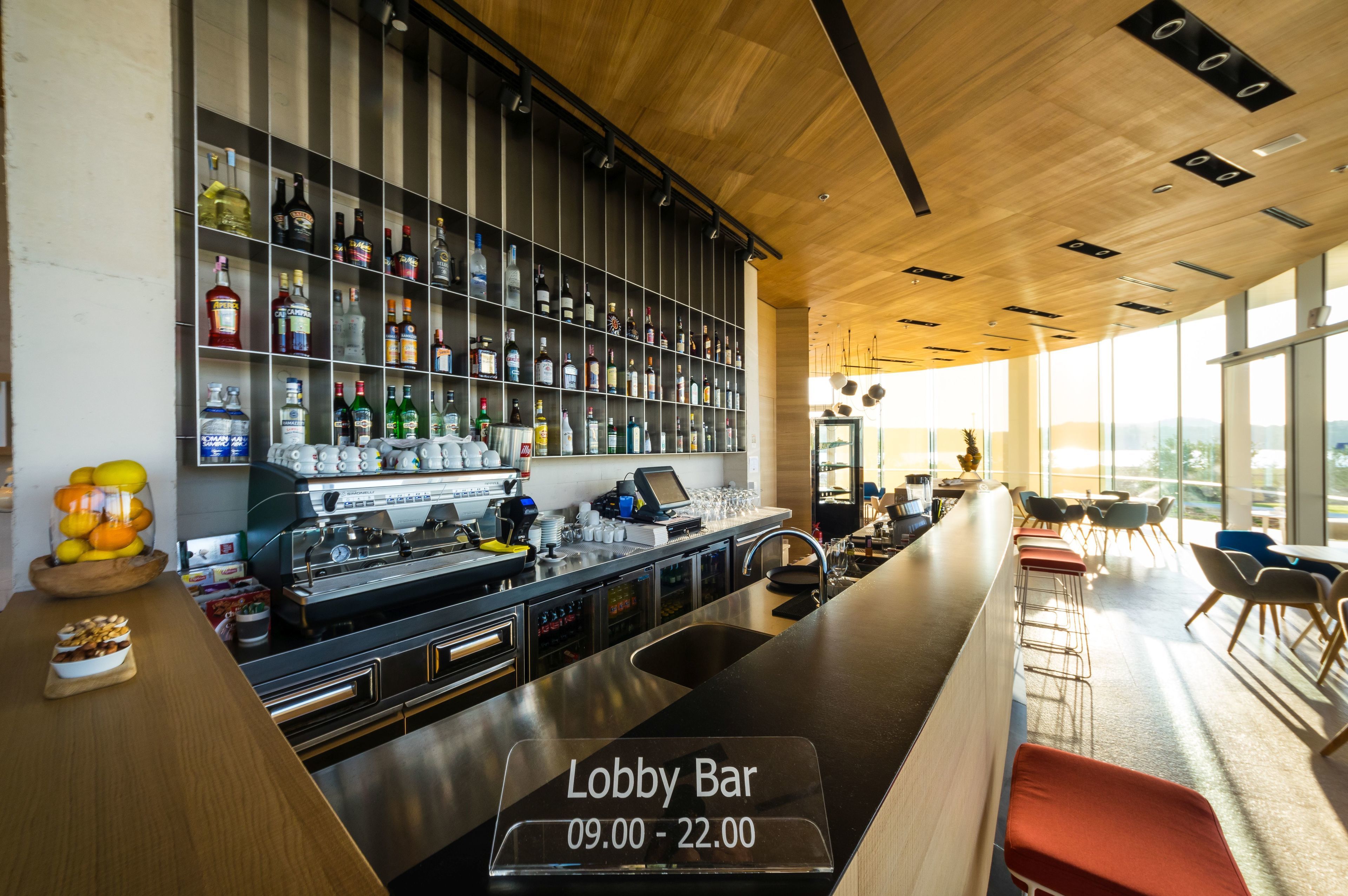 Eine Lobbybar mit Regalen voller Spirituosenflaschen, einer Kasse und einer Sitzgelegenheit mit Tischen und Stühlen.