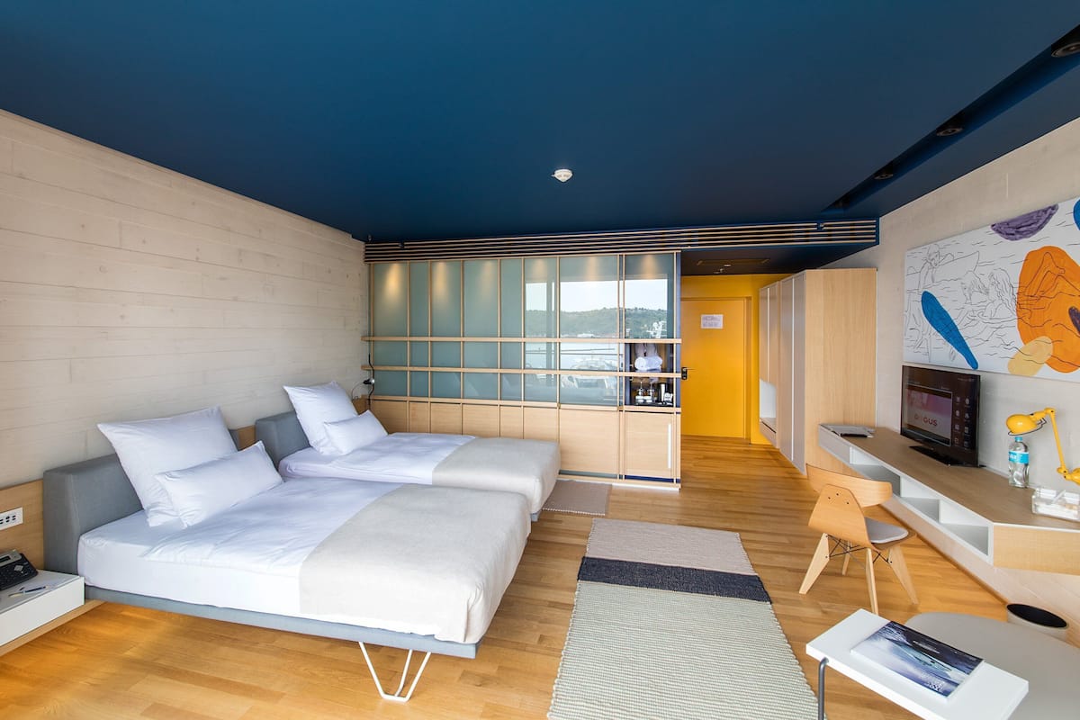 A modern hotel room with a large bed, a desk, and a kitchenette.