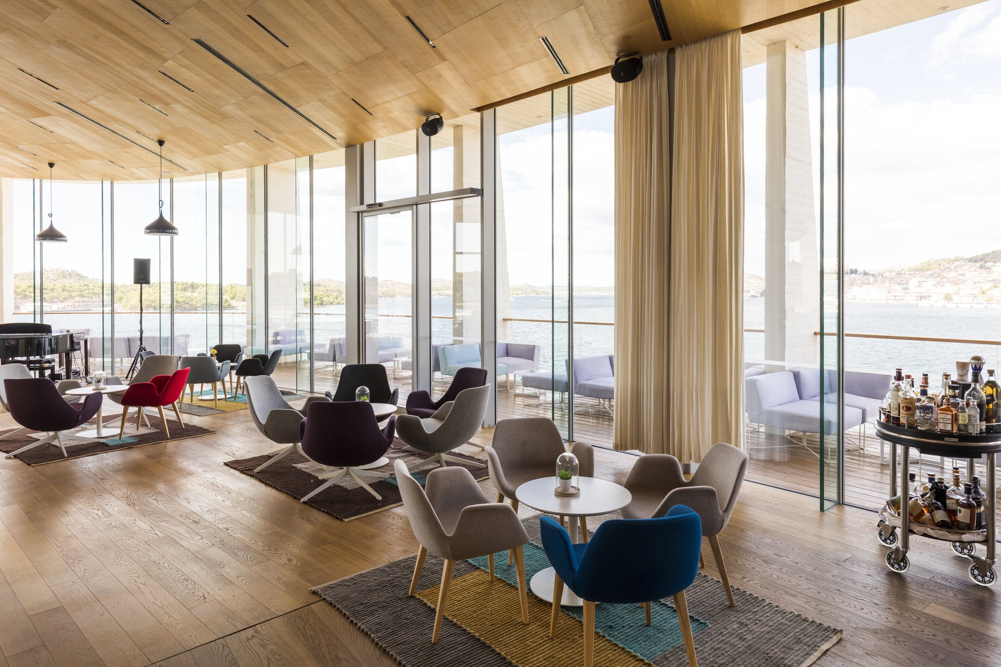 A modern lounge area with large windows, wooden flooring, and a variety of seating options.